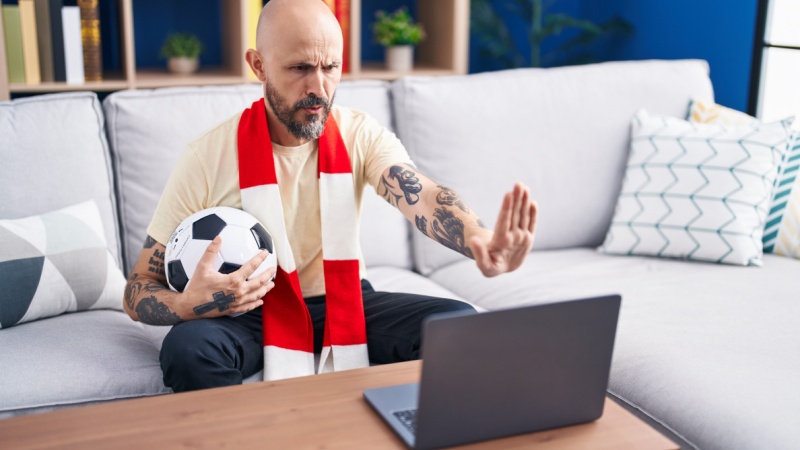 Tifoso con pallone guarda partita sul computer